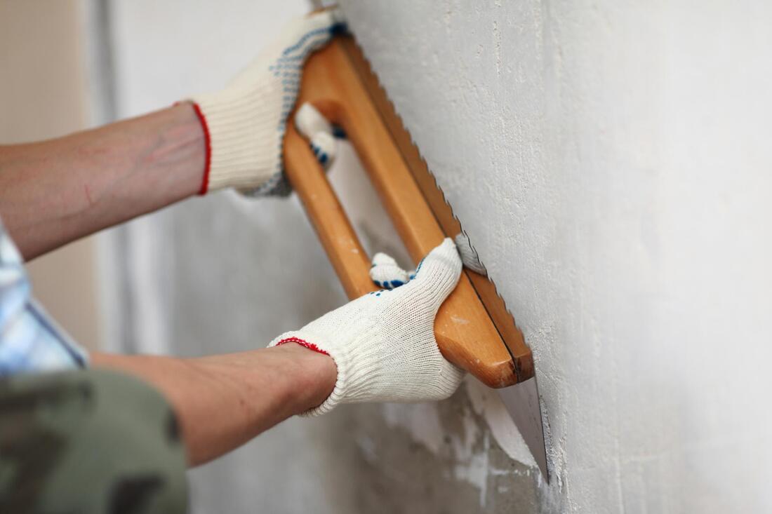 man wearing a gloves and using a plastering tool on a wall
